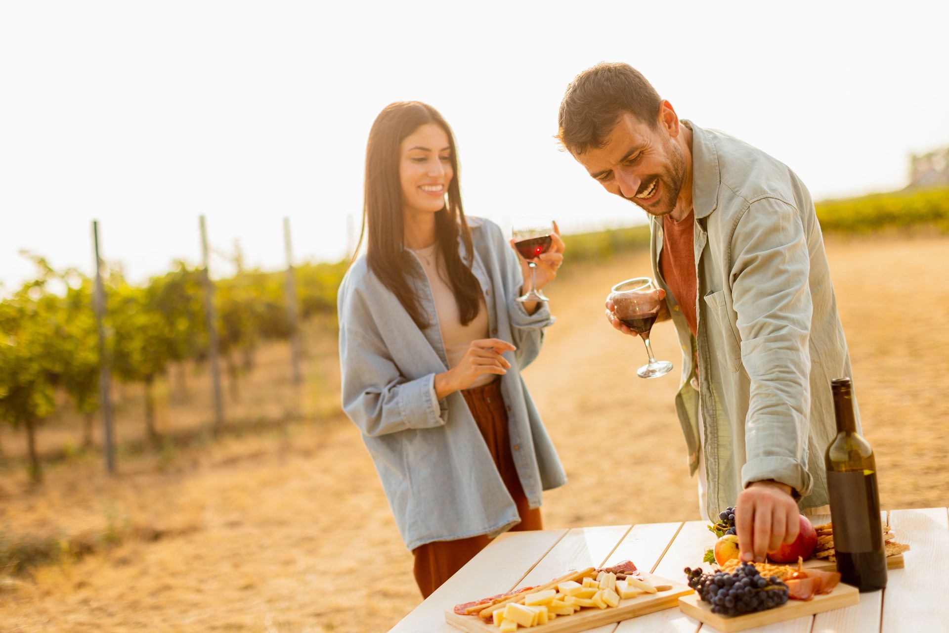 Couple enjoying a sunny afternoon with wine, cheese, and fresh fruits in a picturesque vineyard at golden hour